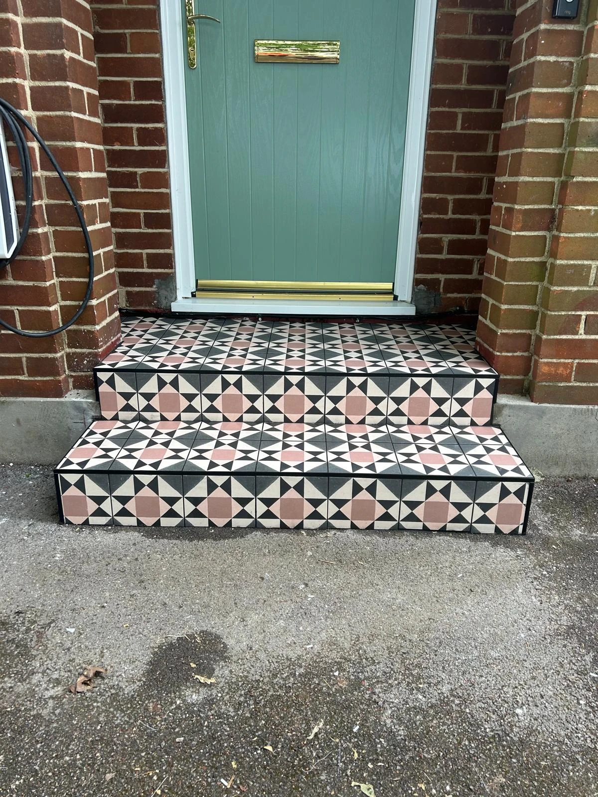 Decorative tiled steps leading to a green front door, featuring geometric patterns in black, pink, and cream.
